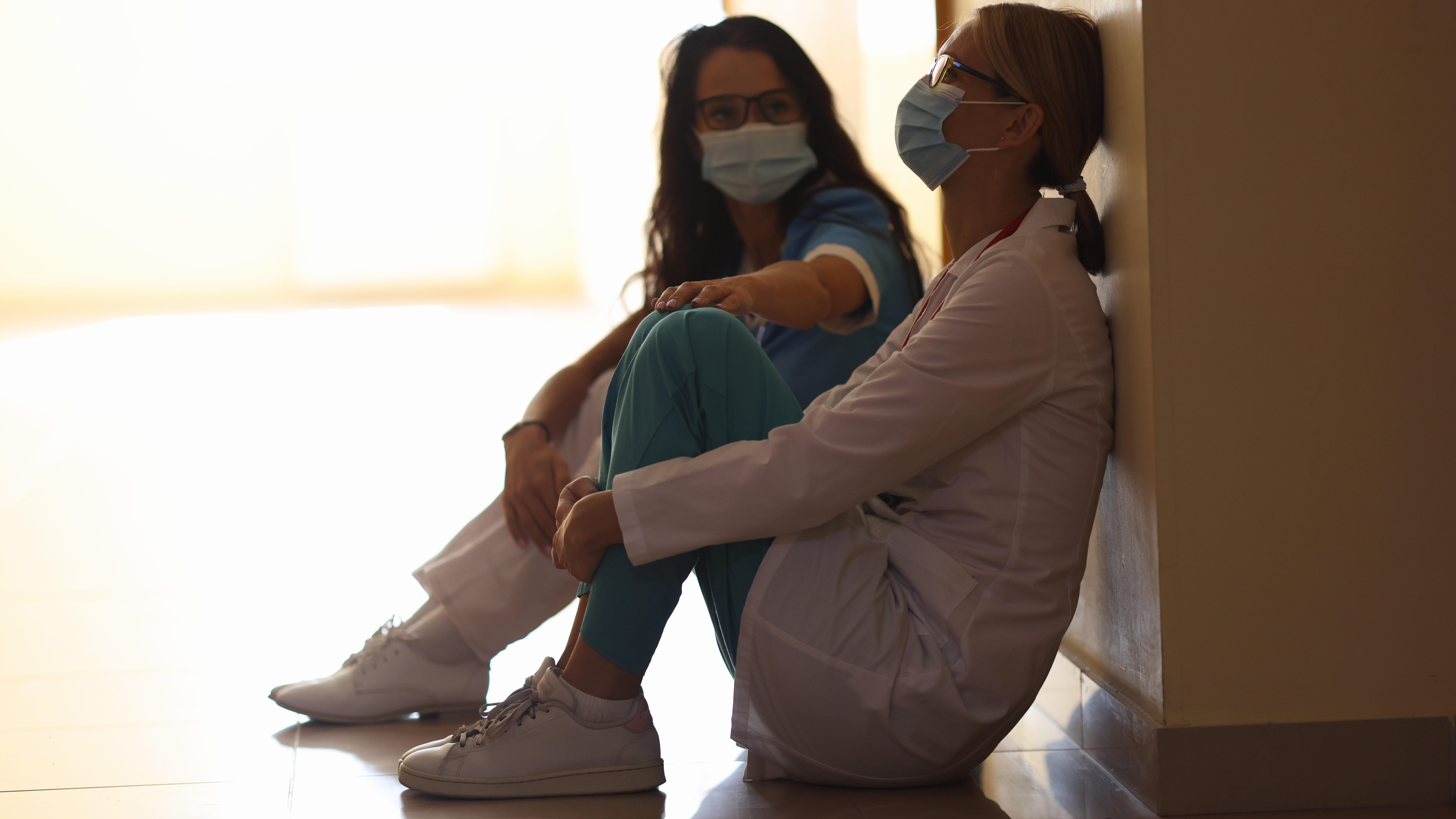 Two women healthcare workers are sitting in masks in corridor