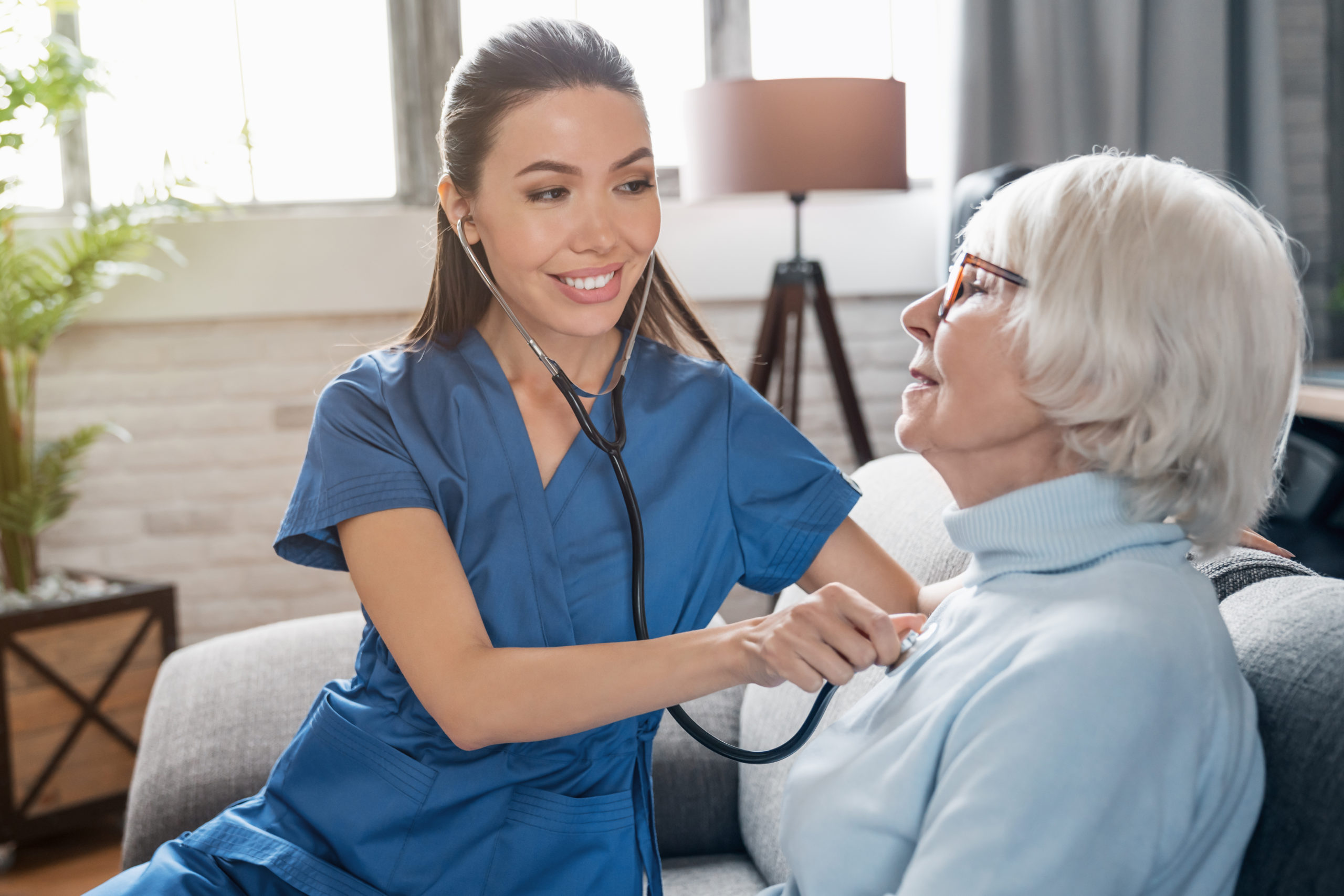 Caring nurse using stethoscope while examining retired woman