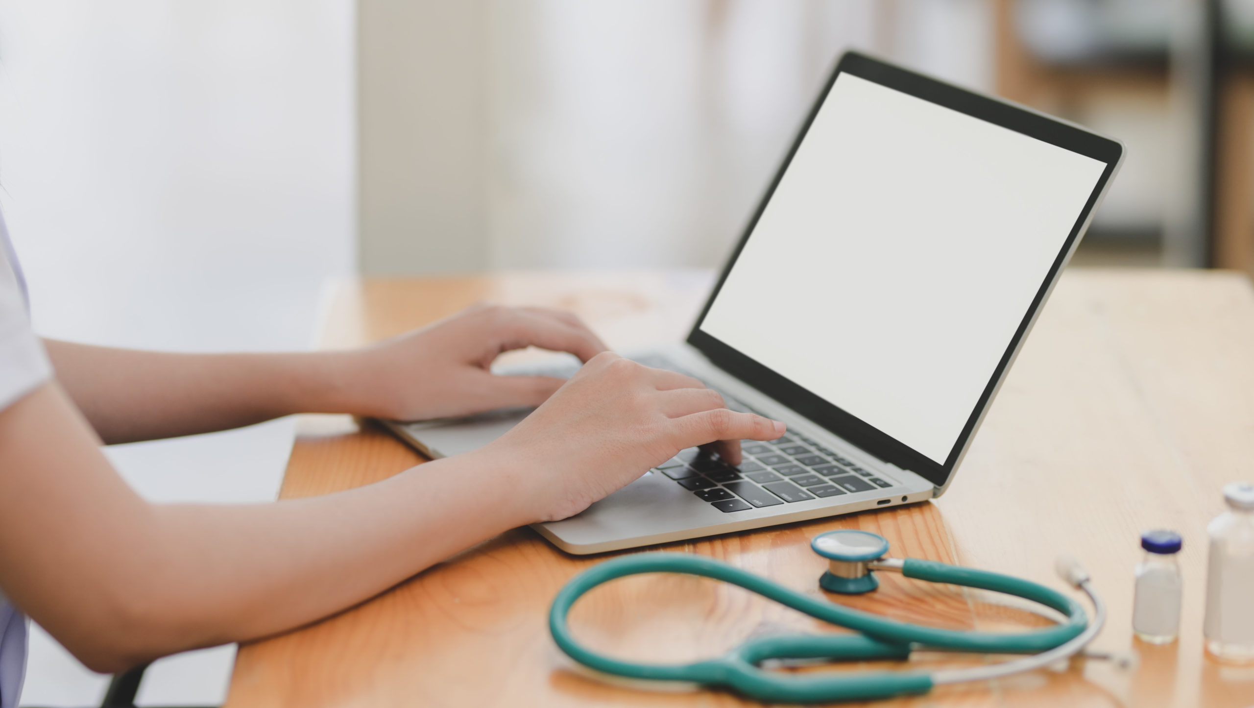 person typing on laptop with a stethoscope on the table