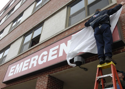 A man covering up an emergency sign on a hospital.