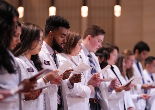 Medical students in white coats reciting a medical oath.